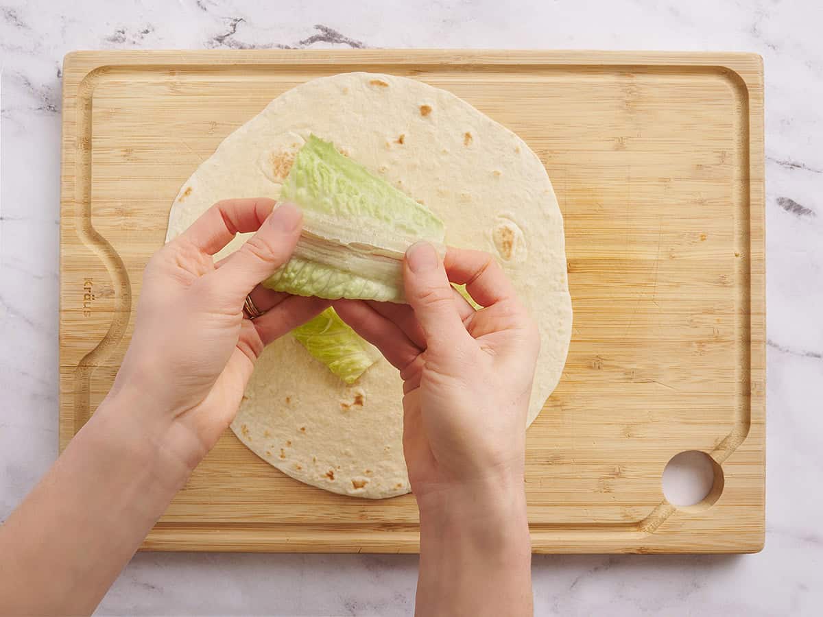 Une main redressant un morceau de laitue avant de le mettre sur un wrap.