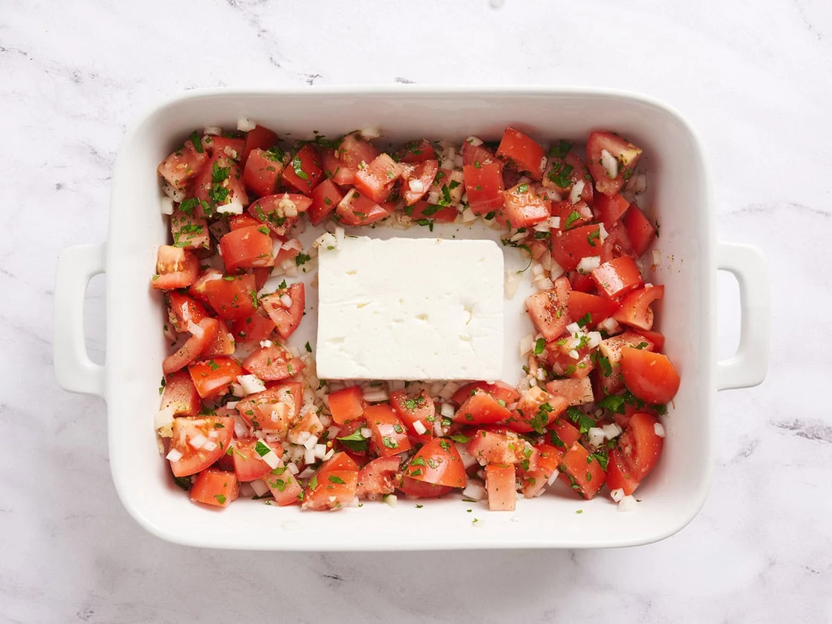 Tomates et oignons coupés en dés dans un plat allant au four avec un bloc de feta au milieu.