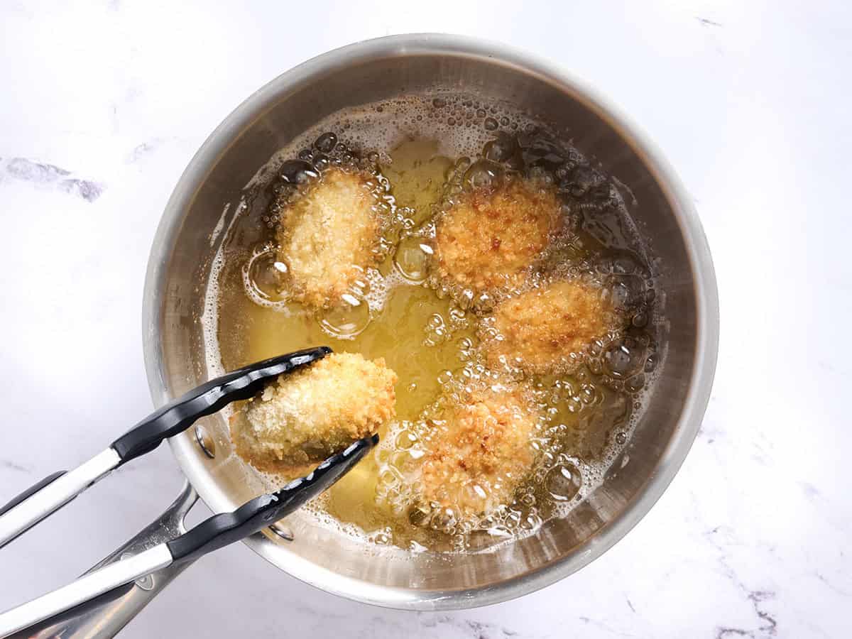 Croquettes de poulet frites dans l'huile avec une pince en retournant une.