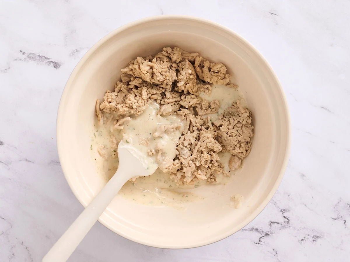 Sauce béchamel ajoutée au poulet haché dans un bol.