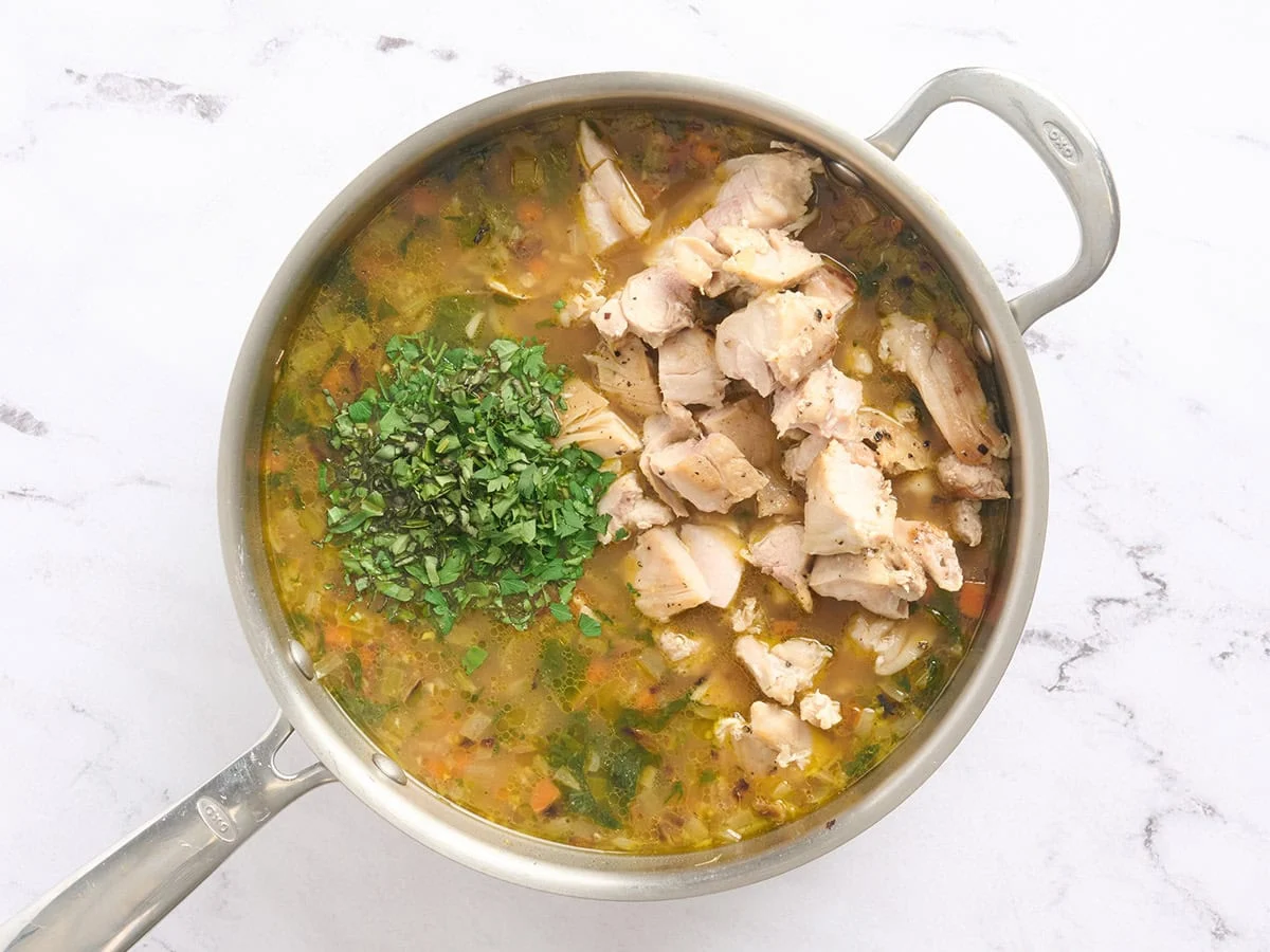 Herbes fraîches et dés de poulet ajoutés à une casserole de bouillon de riz.