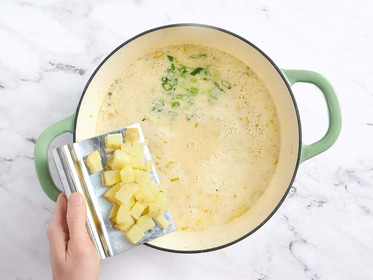 Pommes de terre coupées en dés et oignons verts ajoutés à une casserole de soupe de pommes de terre et poireaux.