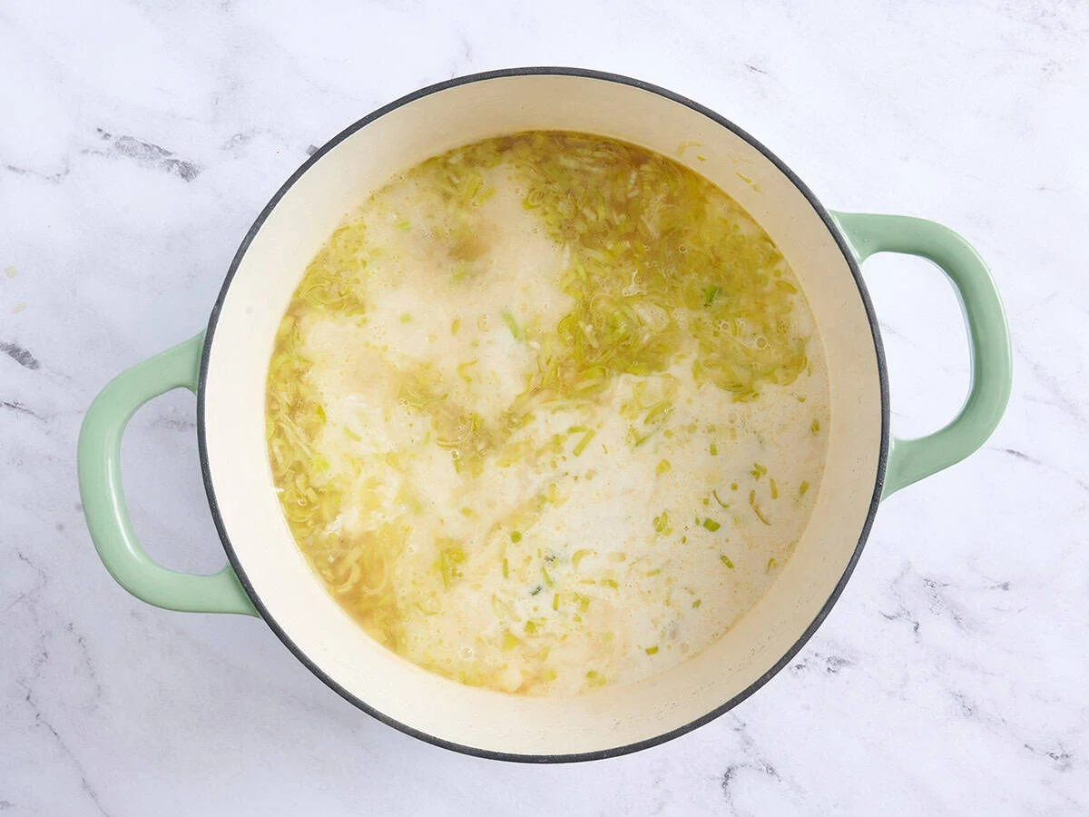 Crème tempérée ajoutée à une soupe de pommes de terre et poireaux dans une casserole.