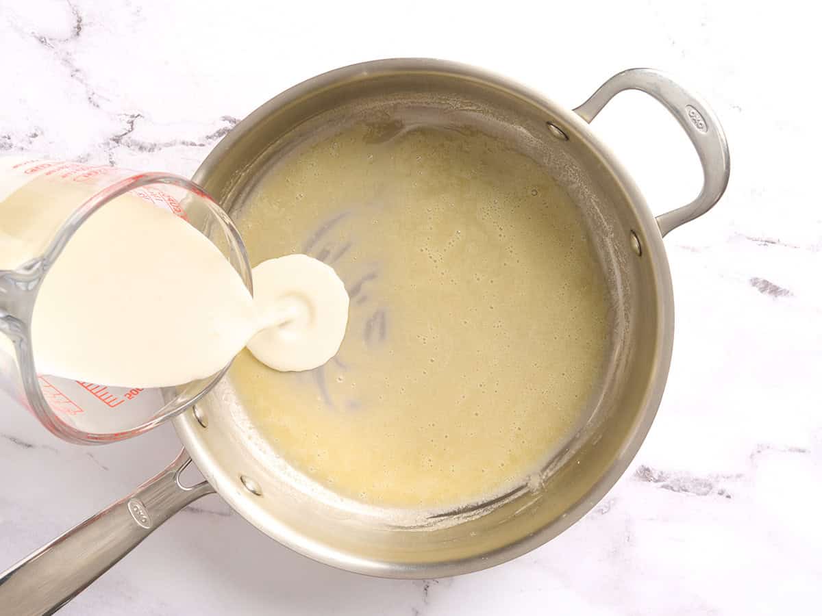 Crème versée dans un roux dans une poêle.