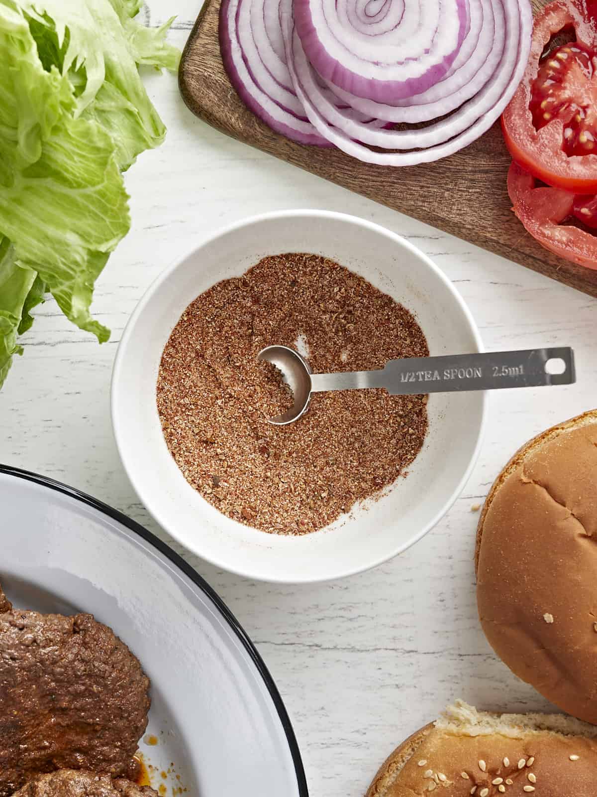 Vue aérienne d'un bol rempli d'assaisonnement pour hamburger entouré de garnitures pour hamburger.