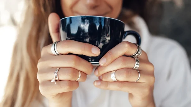 Gros plan main de femme tenant une tasse de café et portant des bagues en argent