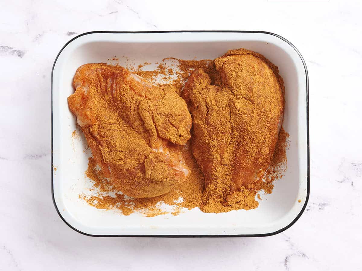 Deux poitrines de poulet recouvertes d'assaisonnement pour tacos dans un plat allant au four.