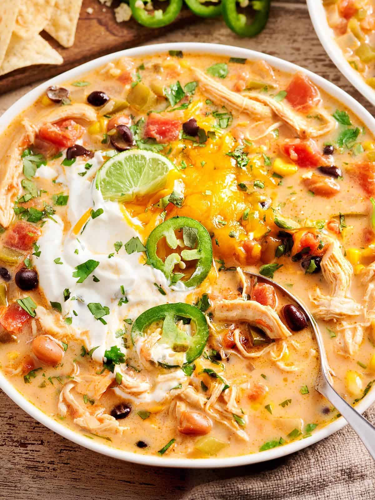 Gros plan de la soupe taco au poulet dans un bol avec une cuillère garnie de tranches de jalapeno et de crème sure.