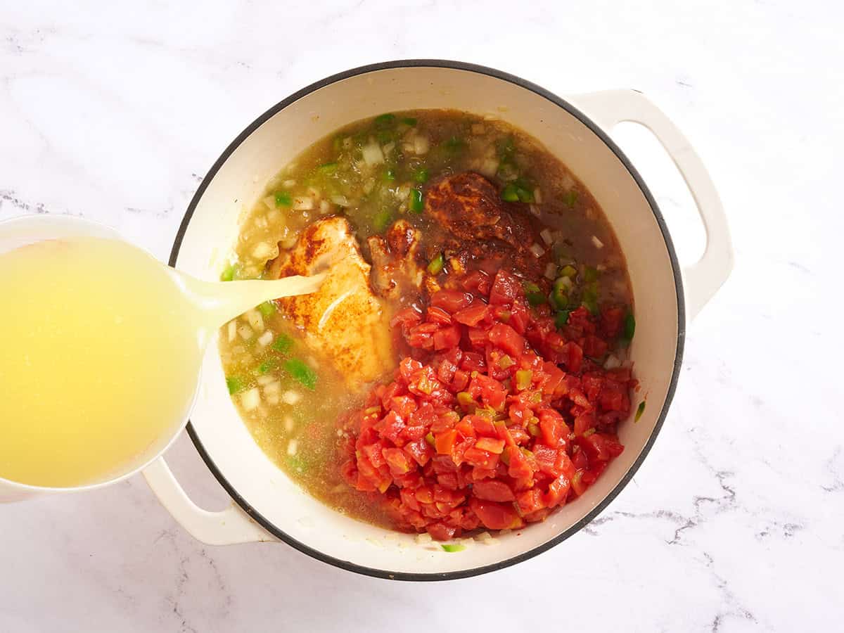 Tomates en conserve avec piments, poitrines de poulet et oignons dans une casserole avec du bouillon de poulet versé.