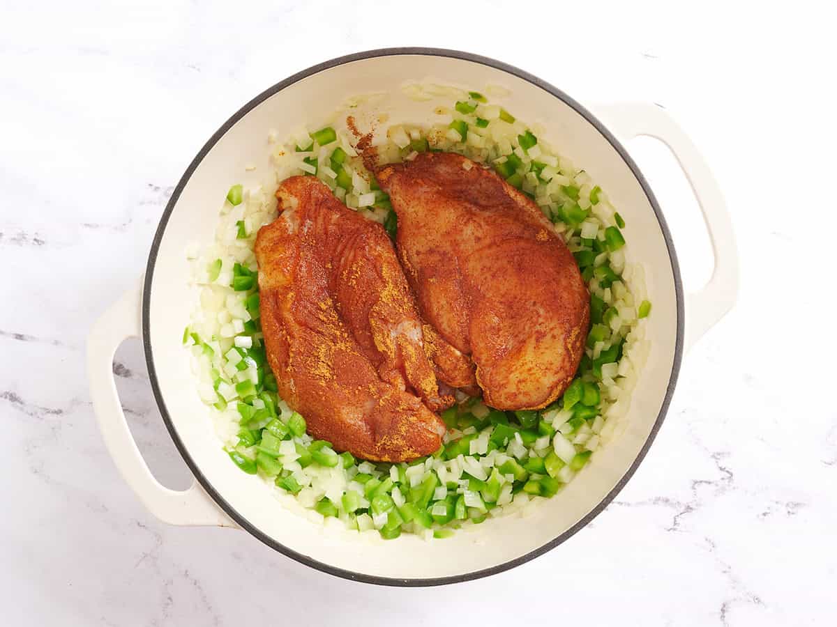 Poitrines de poulet assaisonnées ajoutées à une casserole avec des tranches de poivron vert et des oignons.