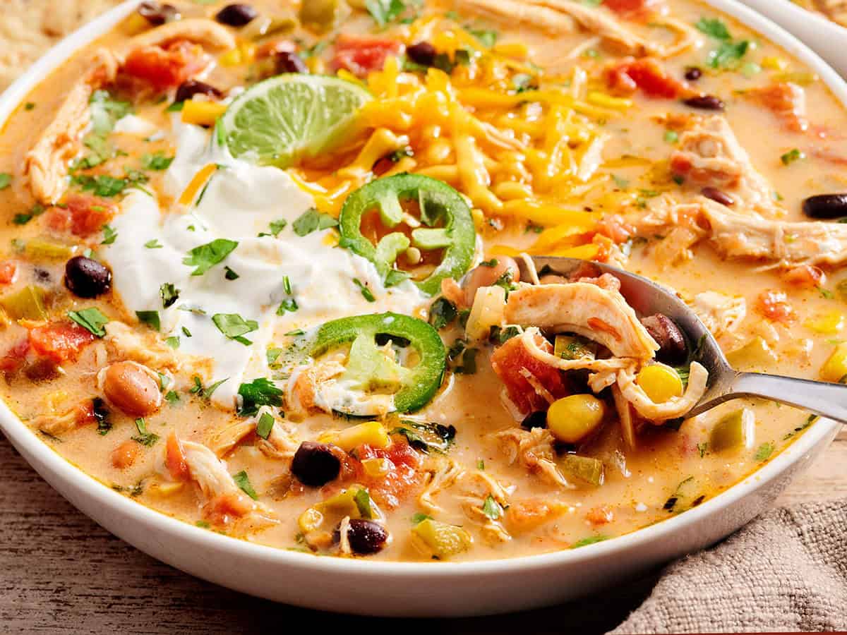 Gros plan de la soupe taco au poulet dans un bol avec une cuillère garnie de tranches de jalapeno et de crème sure.