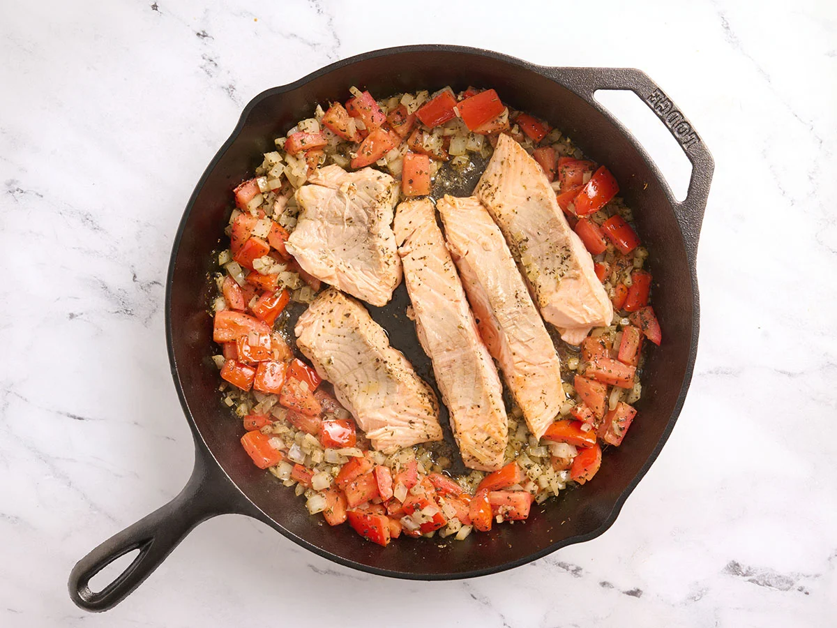Tomates et oignons mis de côté et filets de saumon poêlés au centre d'une poêle.
