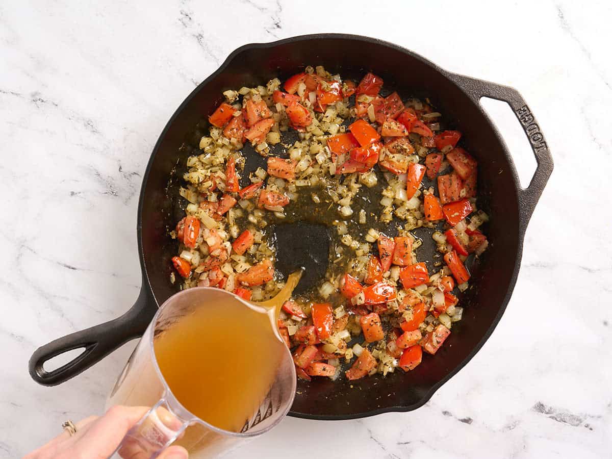 Bouillon de légumes ajouté dans une poêle avec des oignons et des tomates.