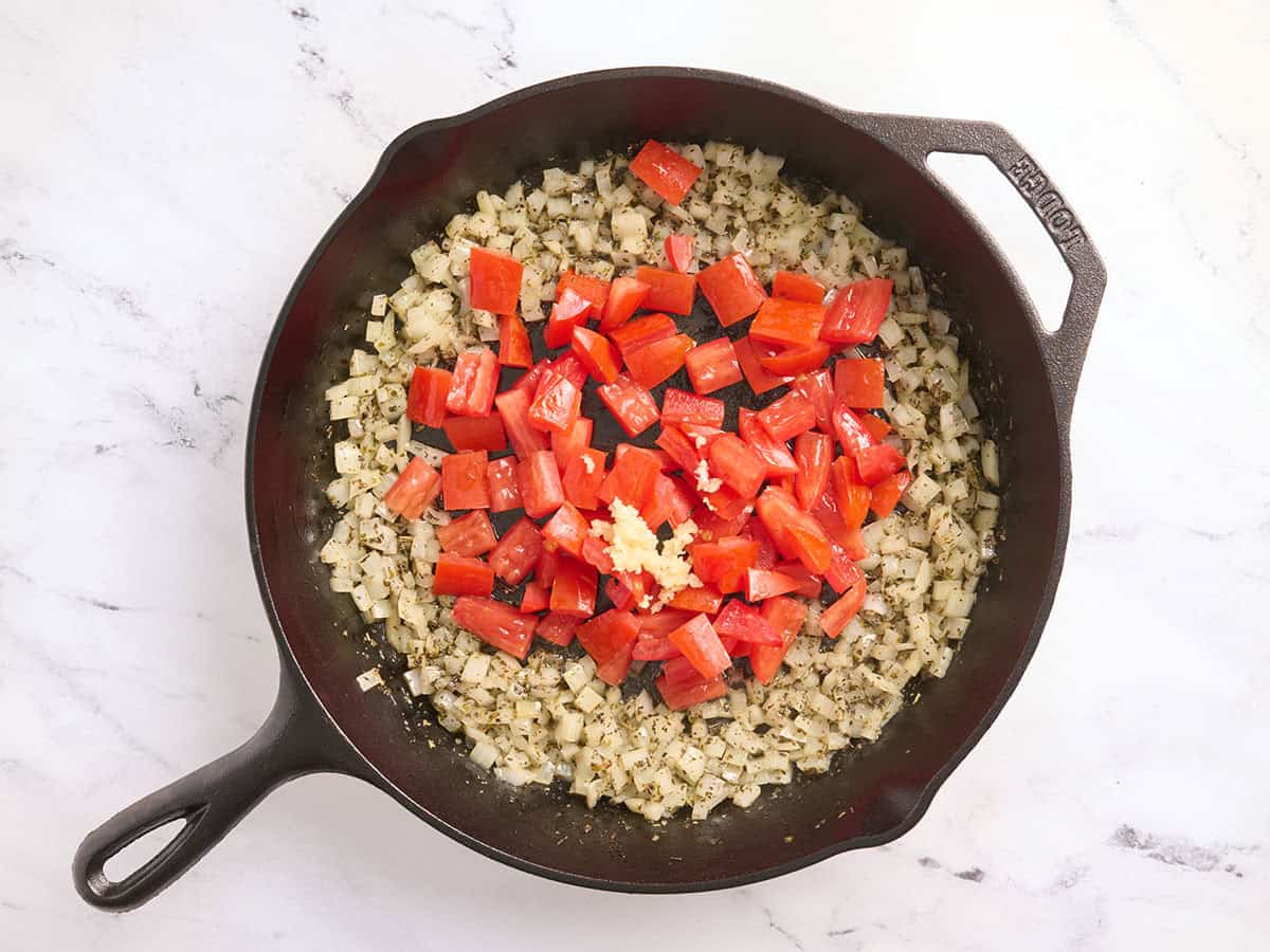 Tomates ajoutées à une poêle avec l'ail et les oignons.
