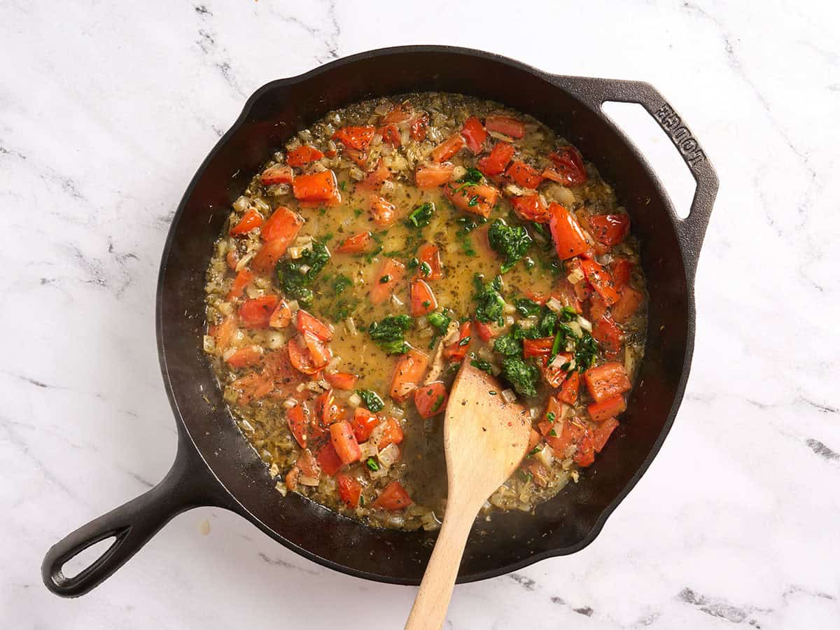Épinards surgelés ajoutés à une poêle avec des tomates, des oignons et du bouillon.