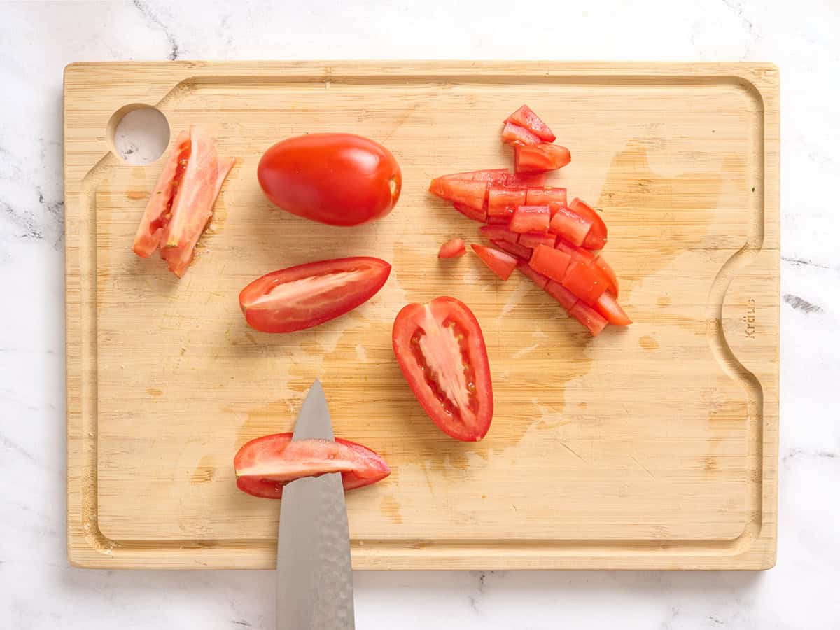 Tomates Roma coupées en quartiers sur une planche à découper en bois, avec un couteau pour enlever les graines.