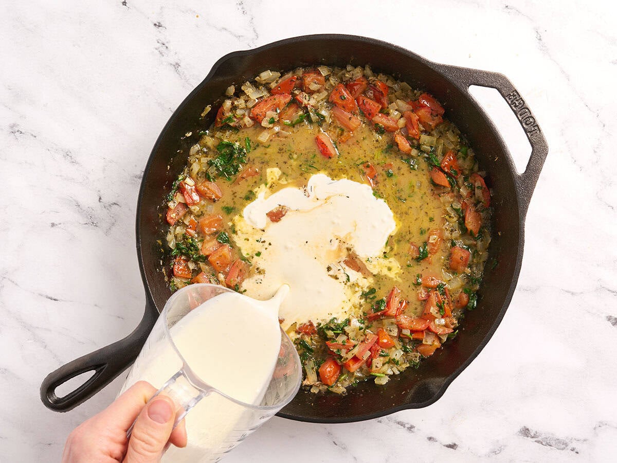 Crème épaisse ajoutée dans une poêle avec oignons, tomates et épinards.