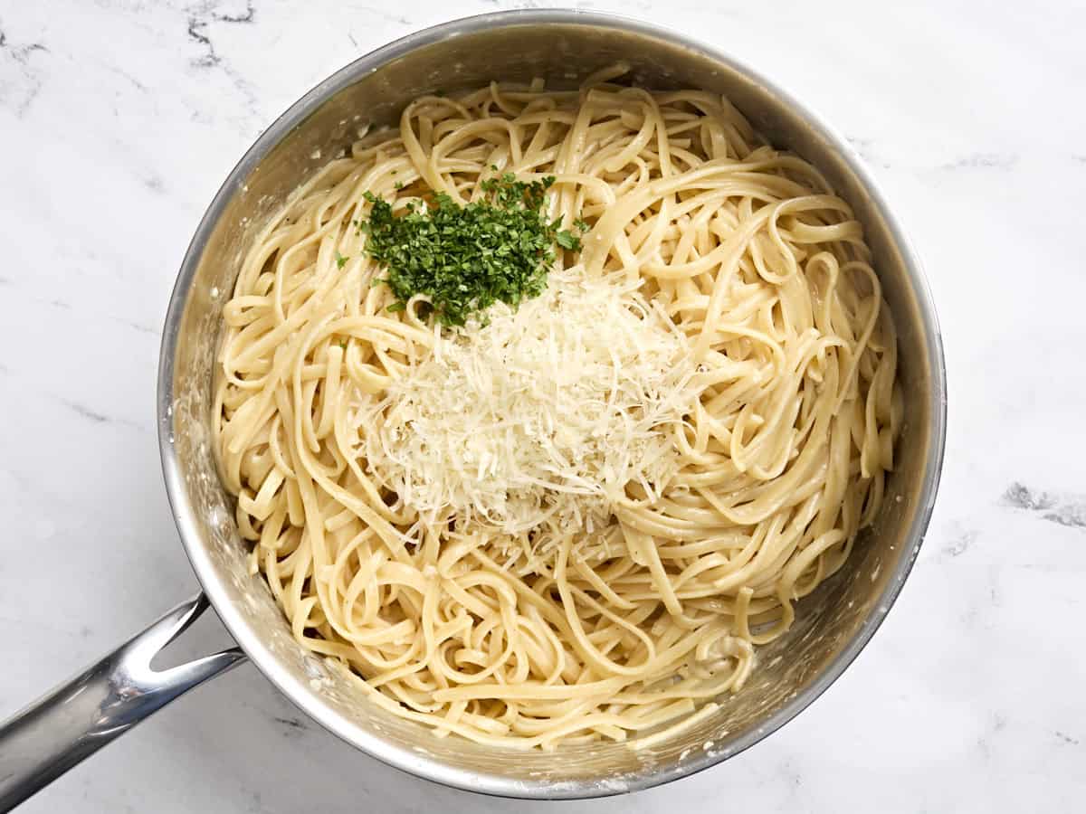 Du parmesan et du persil frais ajoutés à une poêle de Fettuccine Alfredo.