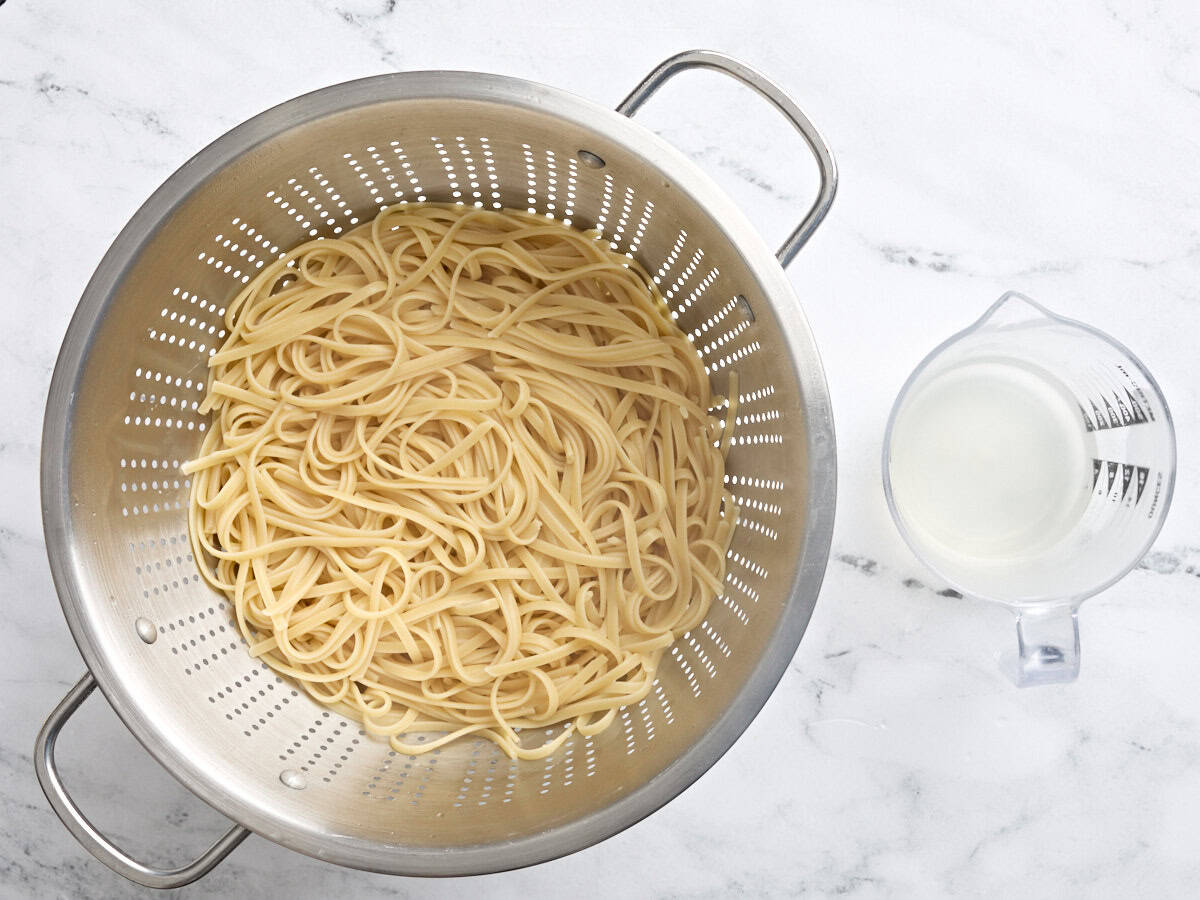 Fettuccine bouillie dans une passoire, à côté d'un pichet en verre d'eau de pâtes réservée.