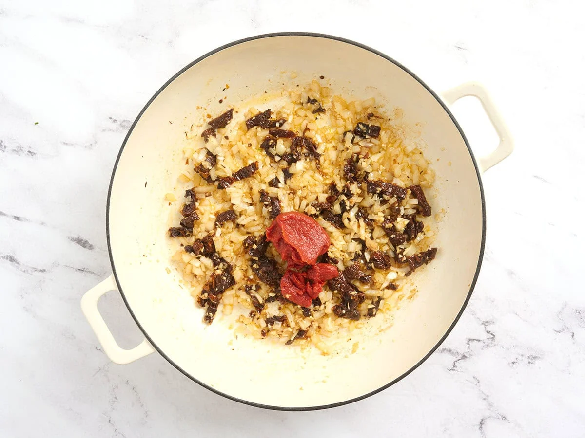 Pâte de tomate ajoutée à une casserole avec des oignons sautés.