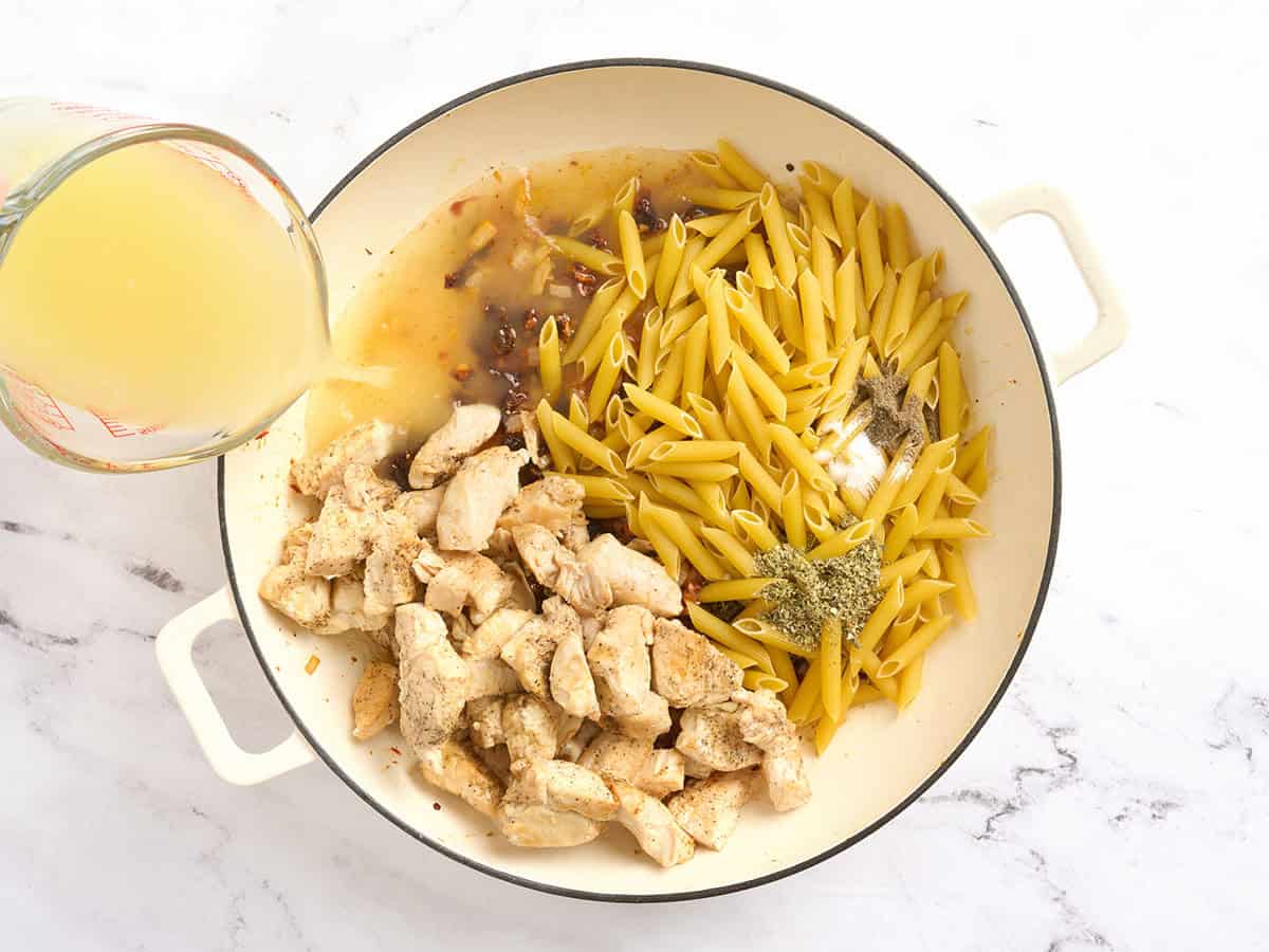 Poulet, bouillon et pâtes ajoutés à une casserole avec des oignons sautés.