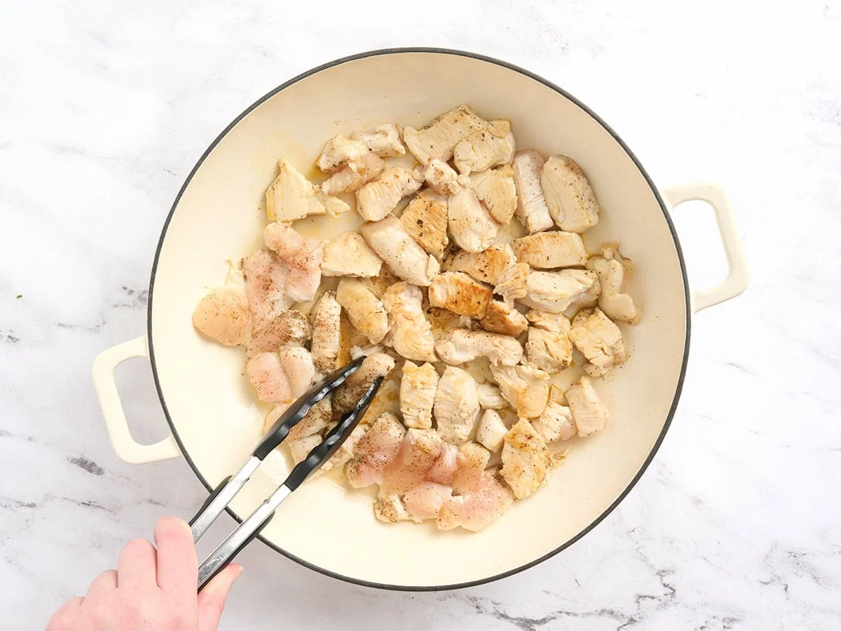 Pinces de cuisine renversant des morceaux de poulet dans une casserole.