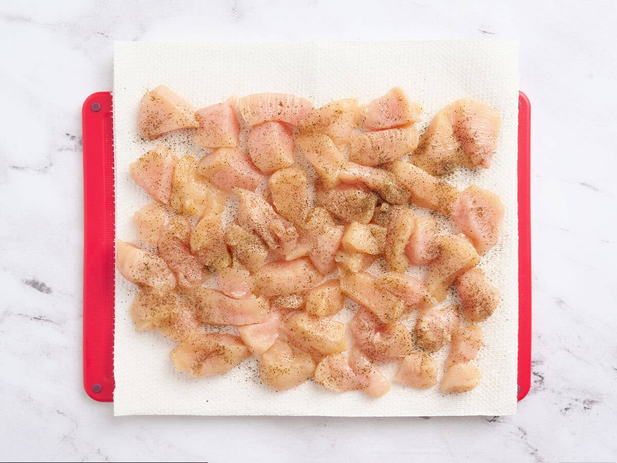 Poulet coupé en dés sur une planche à découper.