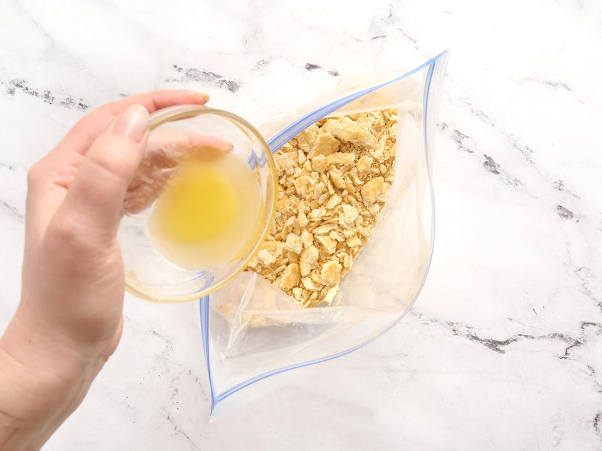 Un sac zippé contenant des craquelins écrasés et du beurre fondu y est versé.