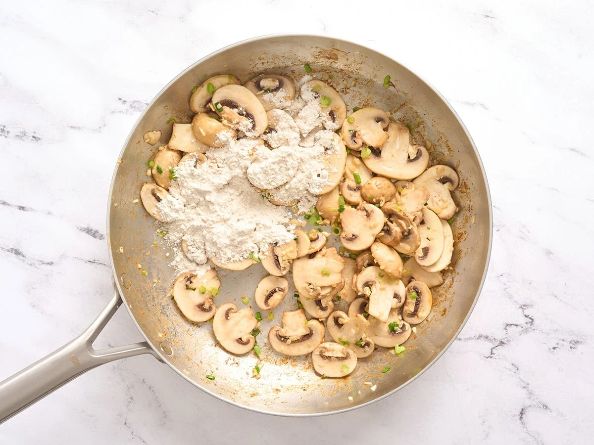 Farine ajoutée aux champignons tranchés dans une poêle.