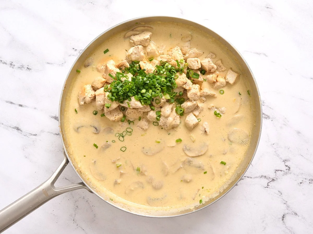 Du poulet et des oignons verts ajoutés à la garniture d'une cocotte de poulet d'un million de dollars dans une poêle.
