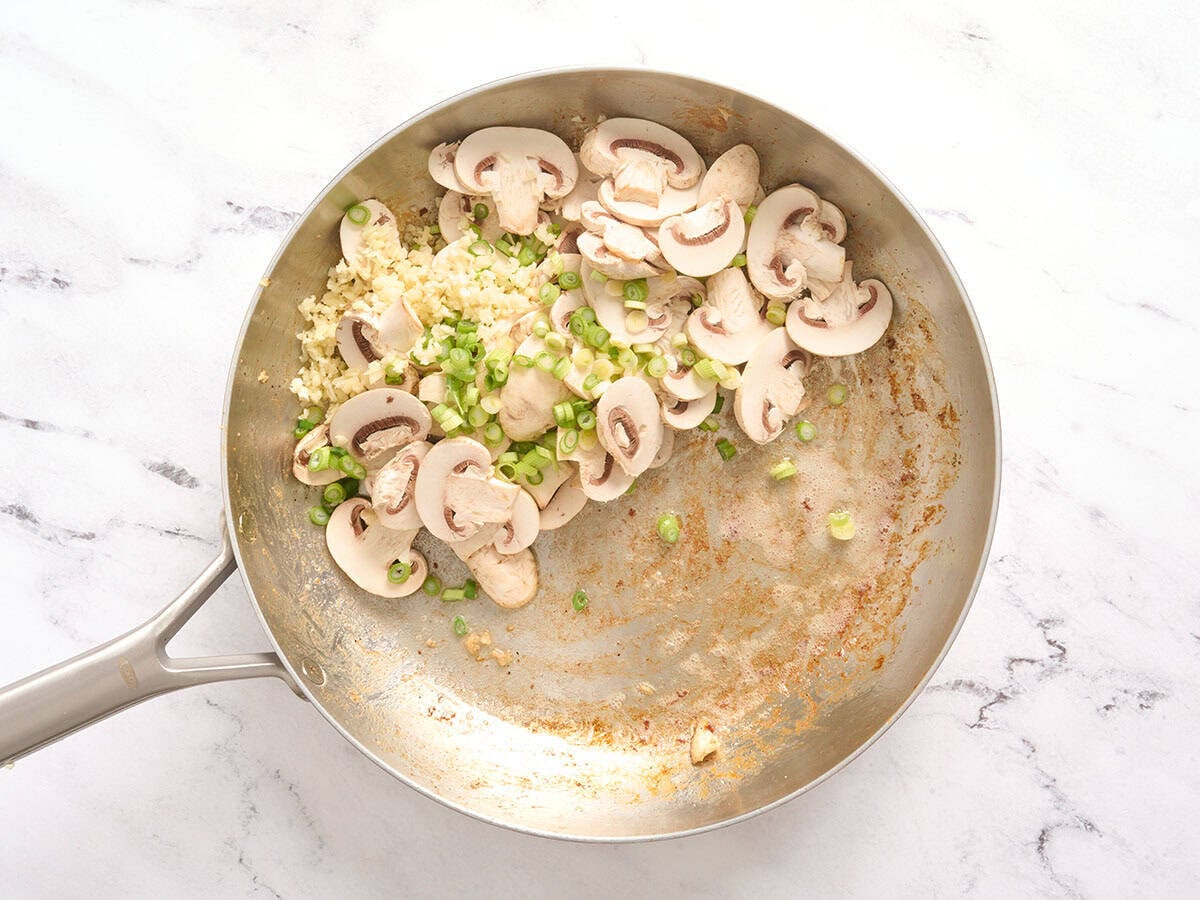 Champignons et oignons verts dans une poêle.
