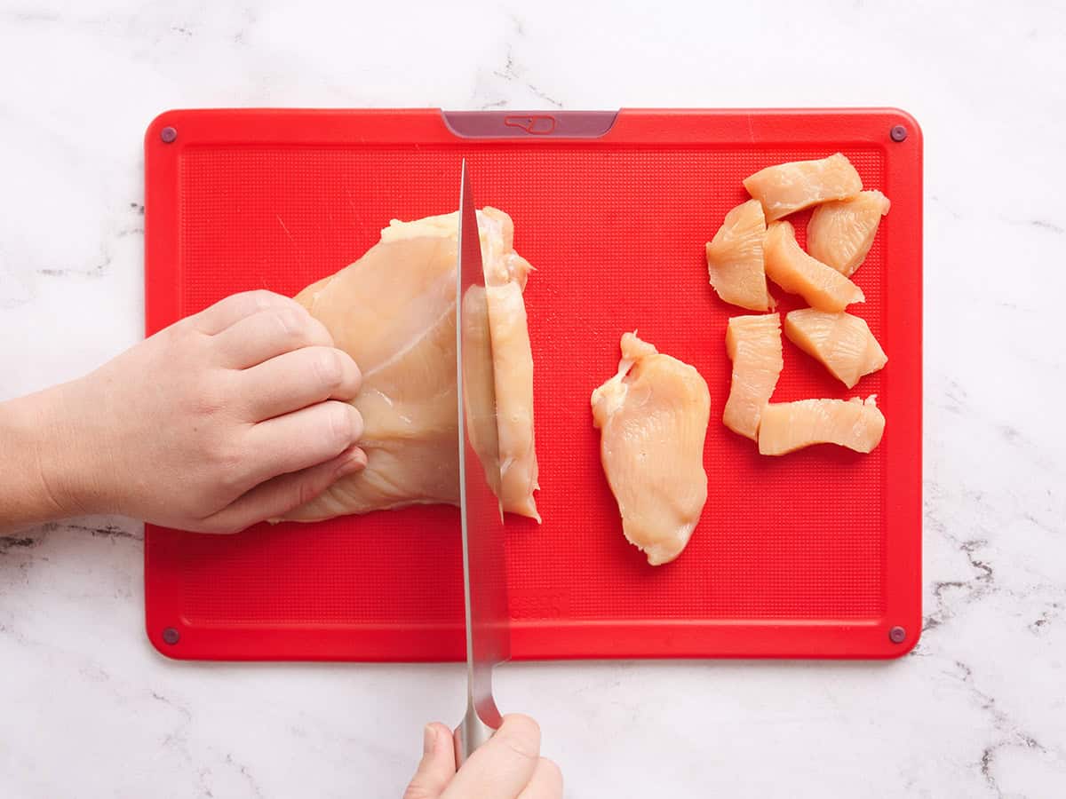 Mains utilisant un couteau pour couper une poitrine de poulet en morceaux.