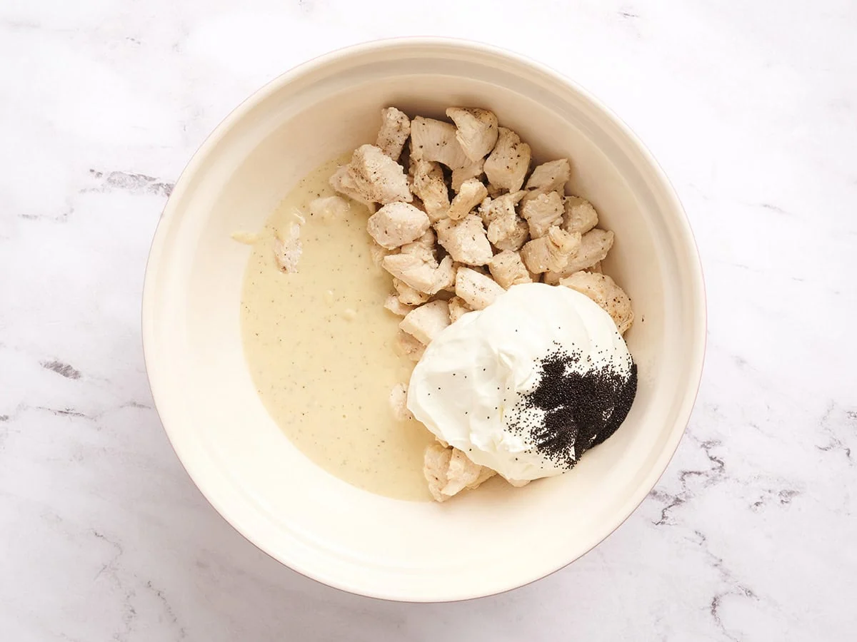 Un bol à mélanger avec du poulet, de la crème sure, des graines de pavot et de la sauce dans un bol.