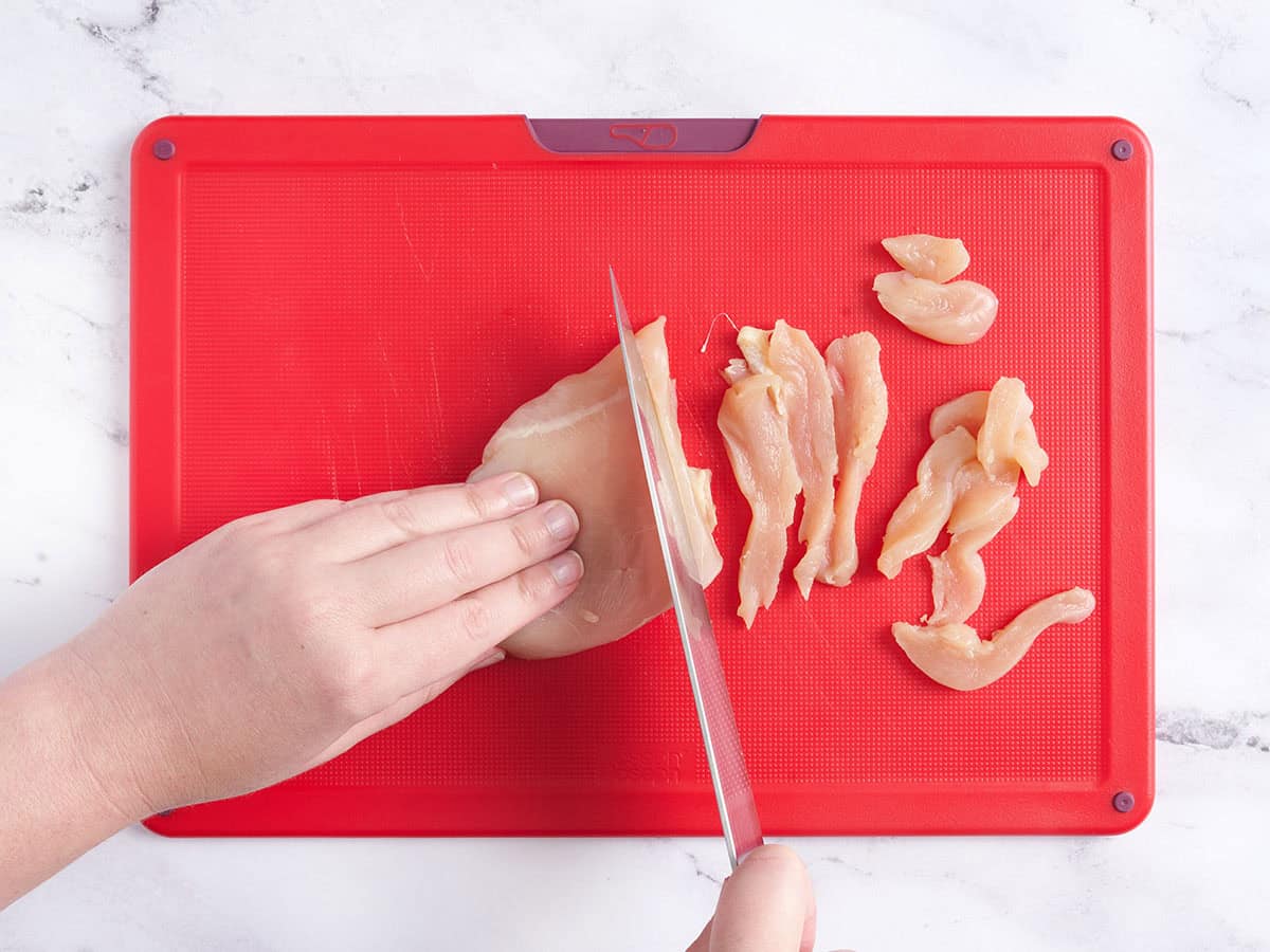 Mains coupant la poitrine de poulet sur une planche à découper.
