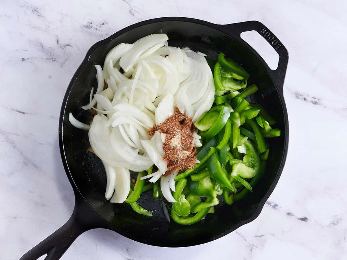 Oignon tranché, poivrons verts et assaisonnement ajoutés dans une poêle.