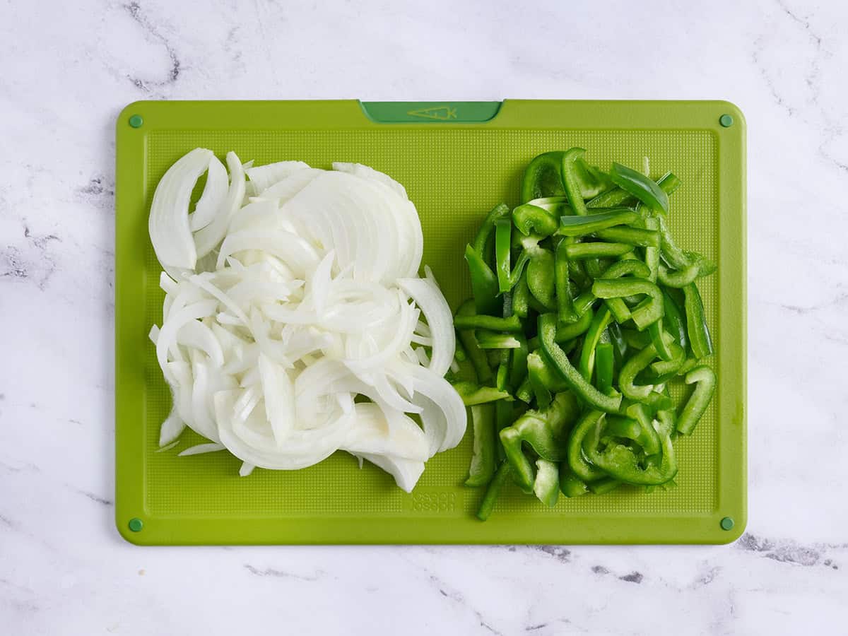 Oignons tranchés et poivrons verts sur une planche à découper.