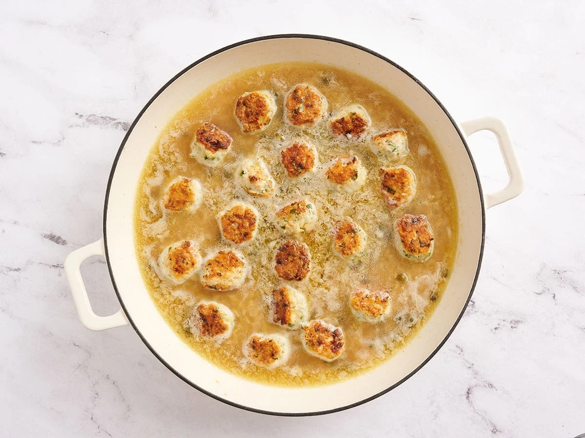 Boulettes de poulet piccata ajoutées à une poêle avec de l'orzo et du bouillon.