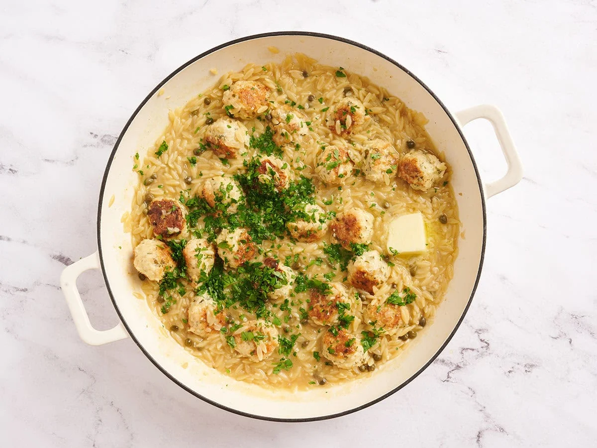 Beurre et persil frais ajoutés à une boulette de poulet piccata et une poêle à l'orzo.