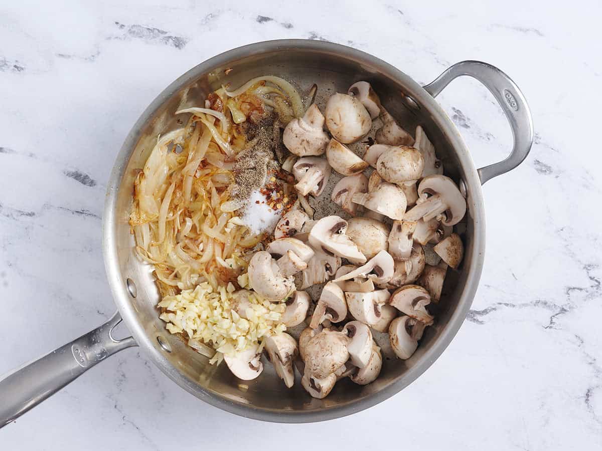 Ail, champignons, oignons caramélisés et assaisonnements dans une poêle.