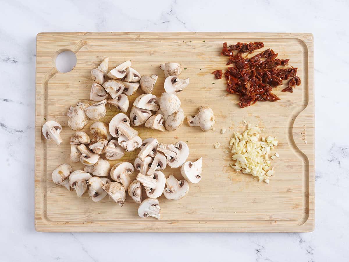 Champignons tranchés, tomates séchées et ail sur une planche à découper en bois.