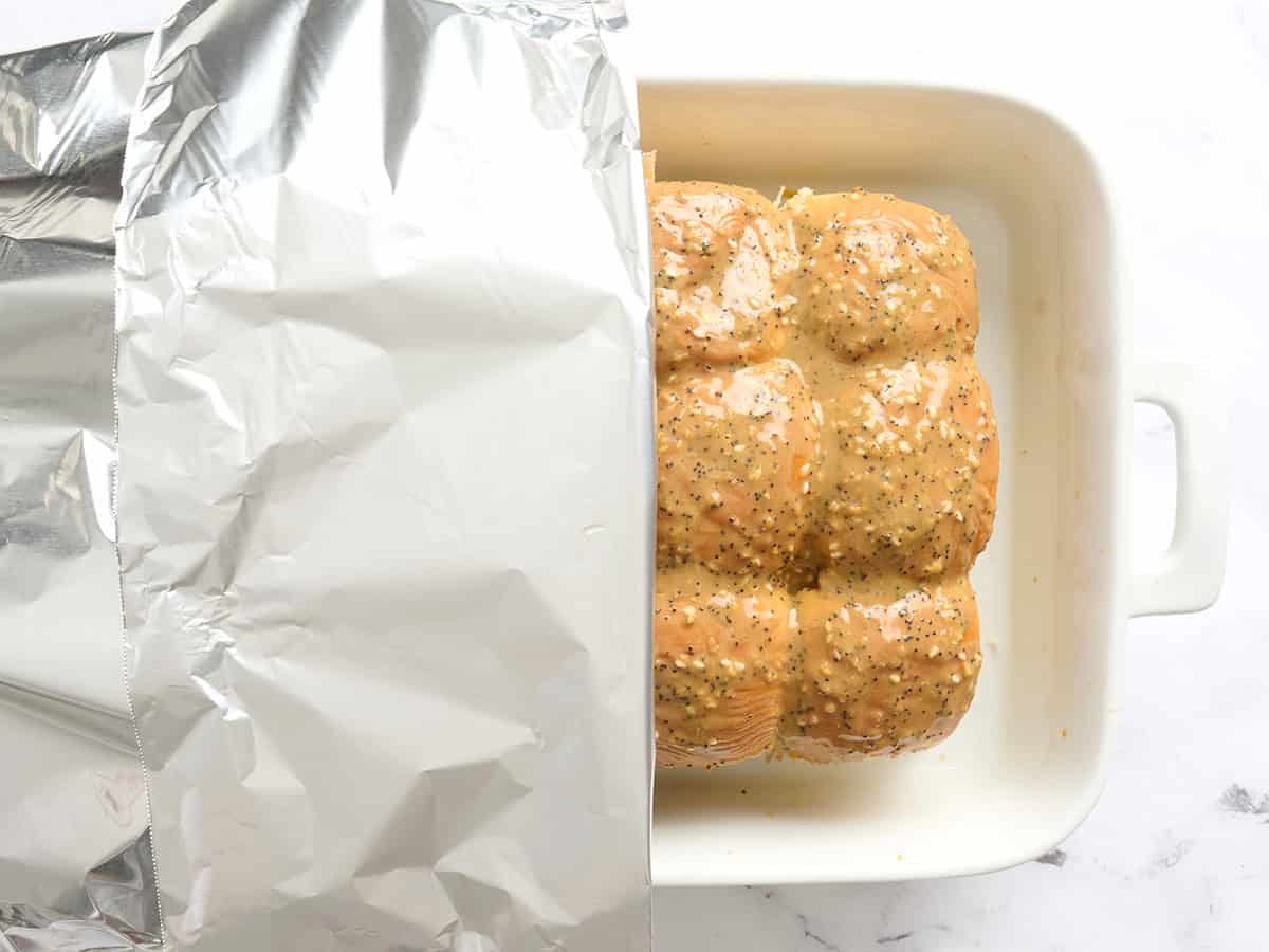 Un plat allant au four composé de sliders de poulet recouverts de papier d'aluminium.