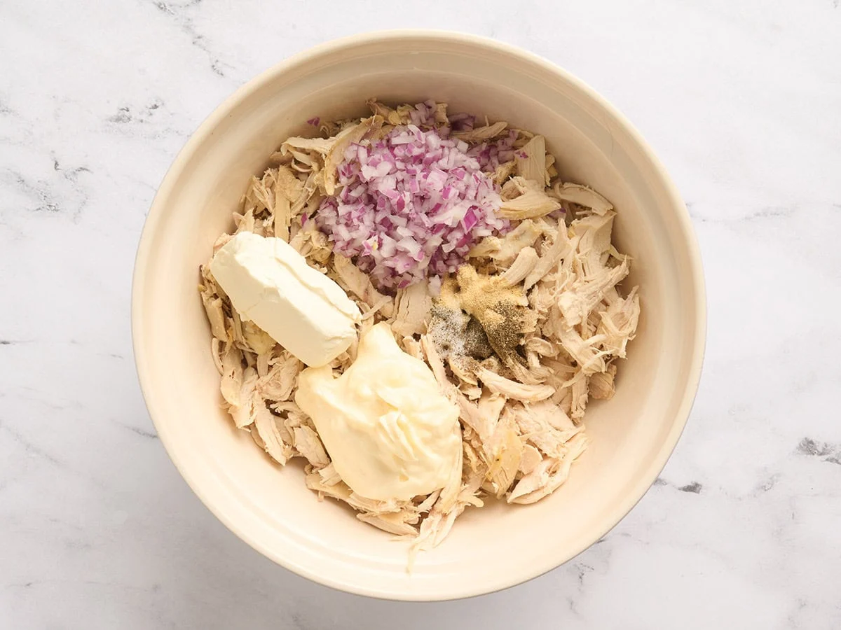 Poulet râpé, oignon rouge coupé en dés, mayonnaise, fromage à la crème et assaisonnements dans un bol à mélanger.