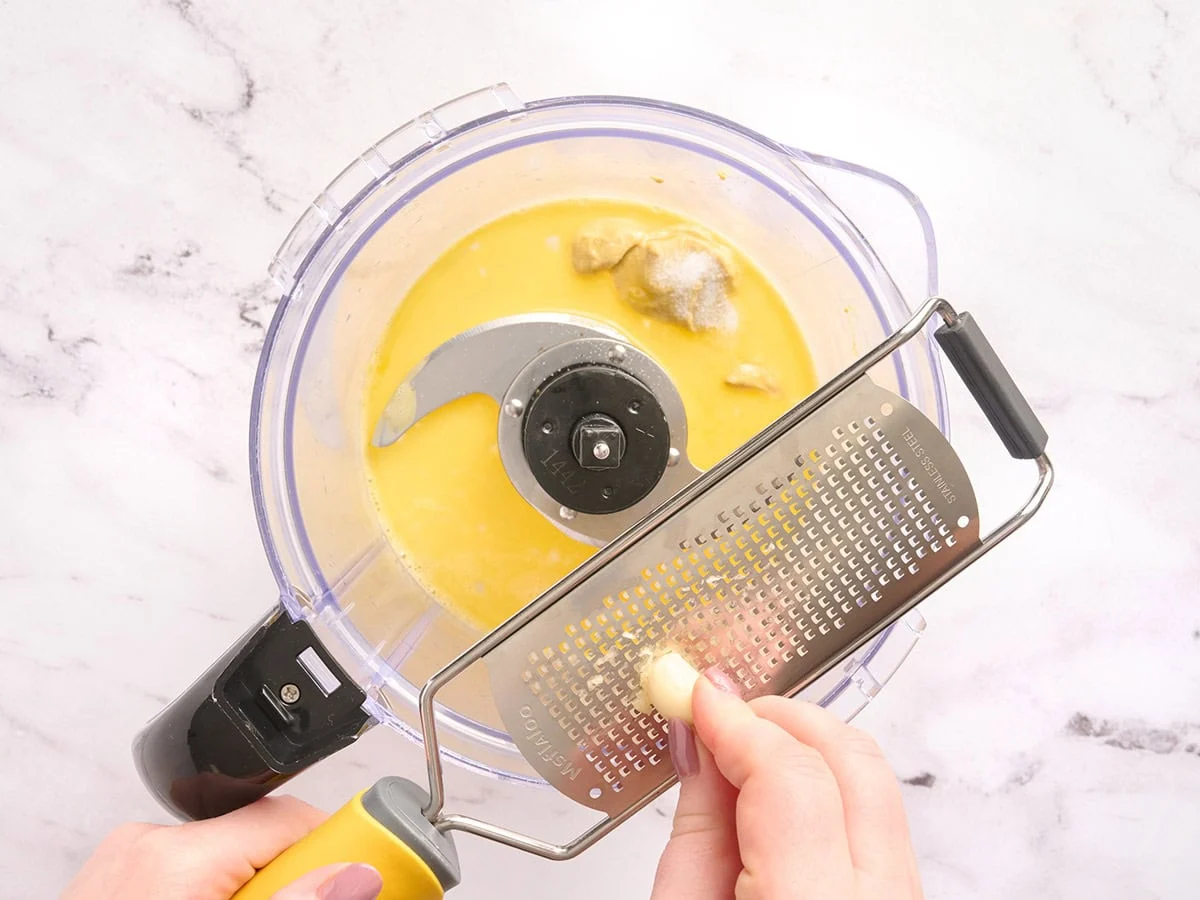 Mains râpant un gant d'ail dans un robot culinaire.