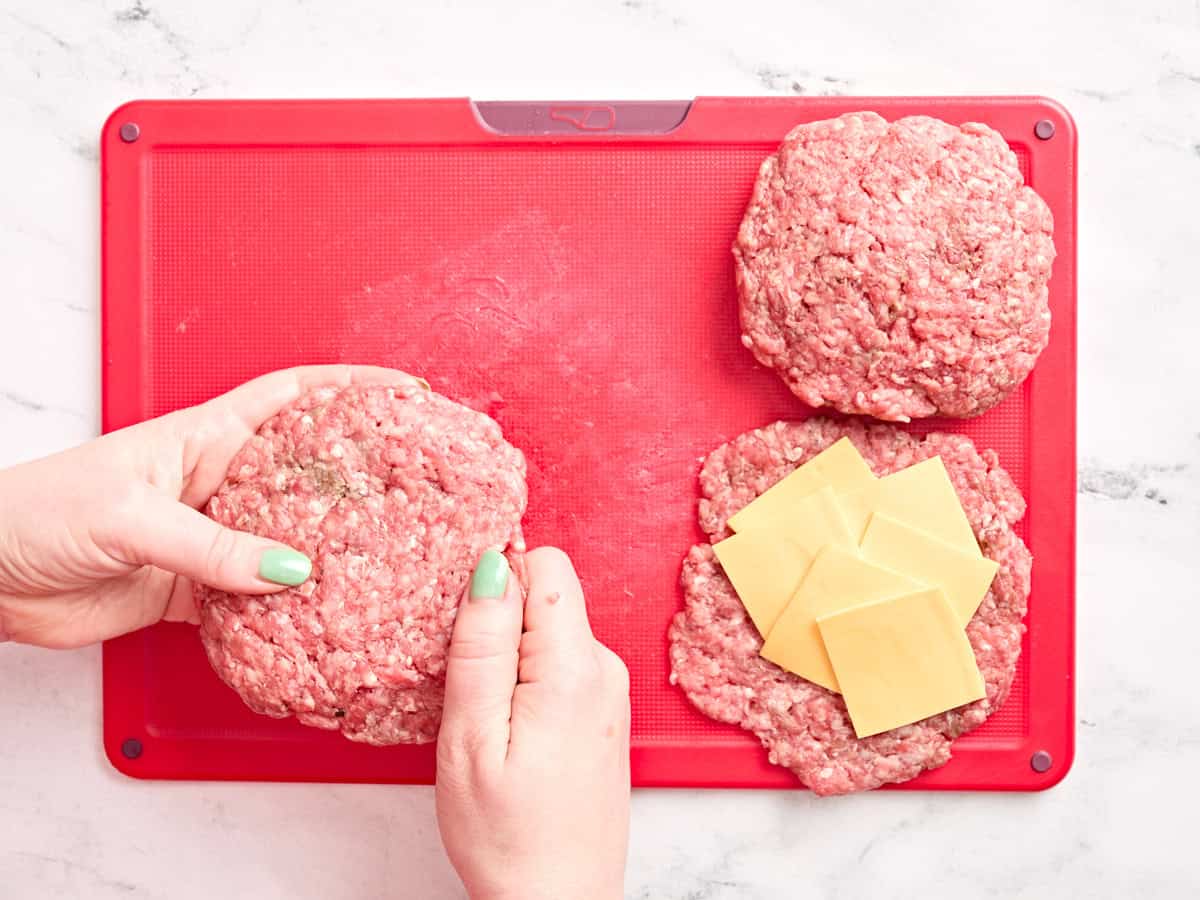 Mains remplissant les galettes de hamburger avec du fromage.