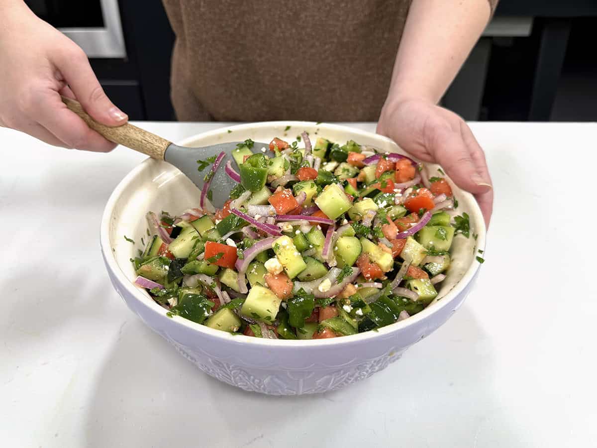 Vue de face de quelqu'un mélangeant une salade de concombre et de tomates dans un bol.