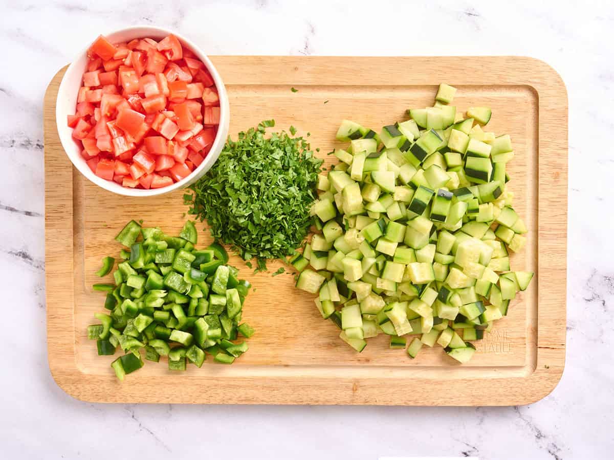 Tomates hachées, poivron vert, concombre et persil sur une planche à découper en bois.