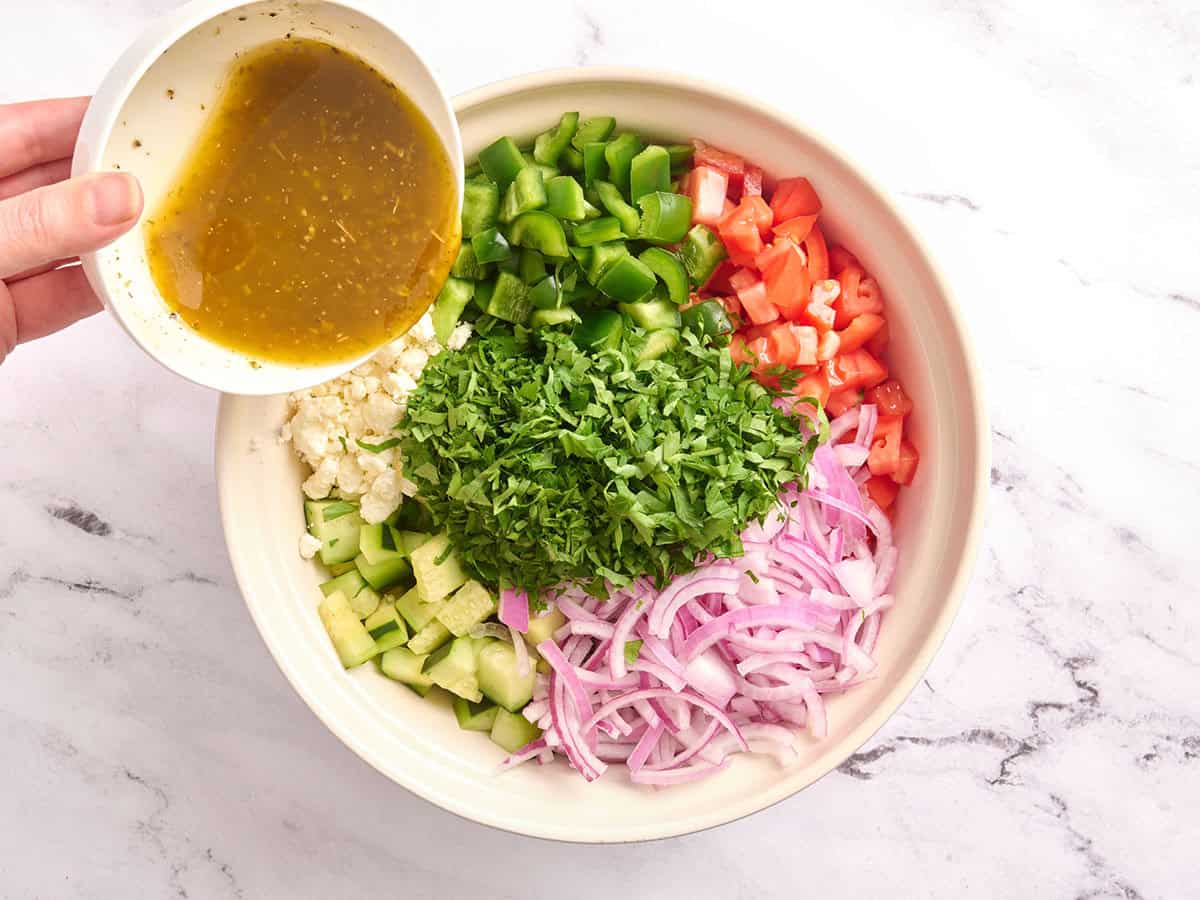 Ingrédients de la salade de concombre et de tomates dans un bol avec la vinaigrette versée dessus.