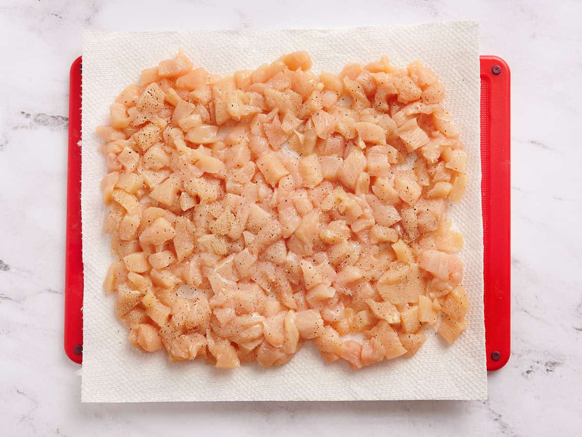 Poulet coupé en dés sur une planche à découper avec du papier sulfurisé.