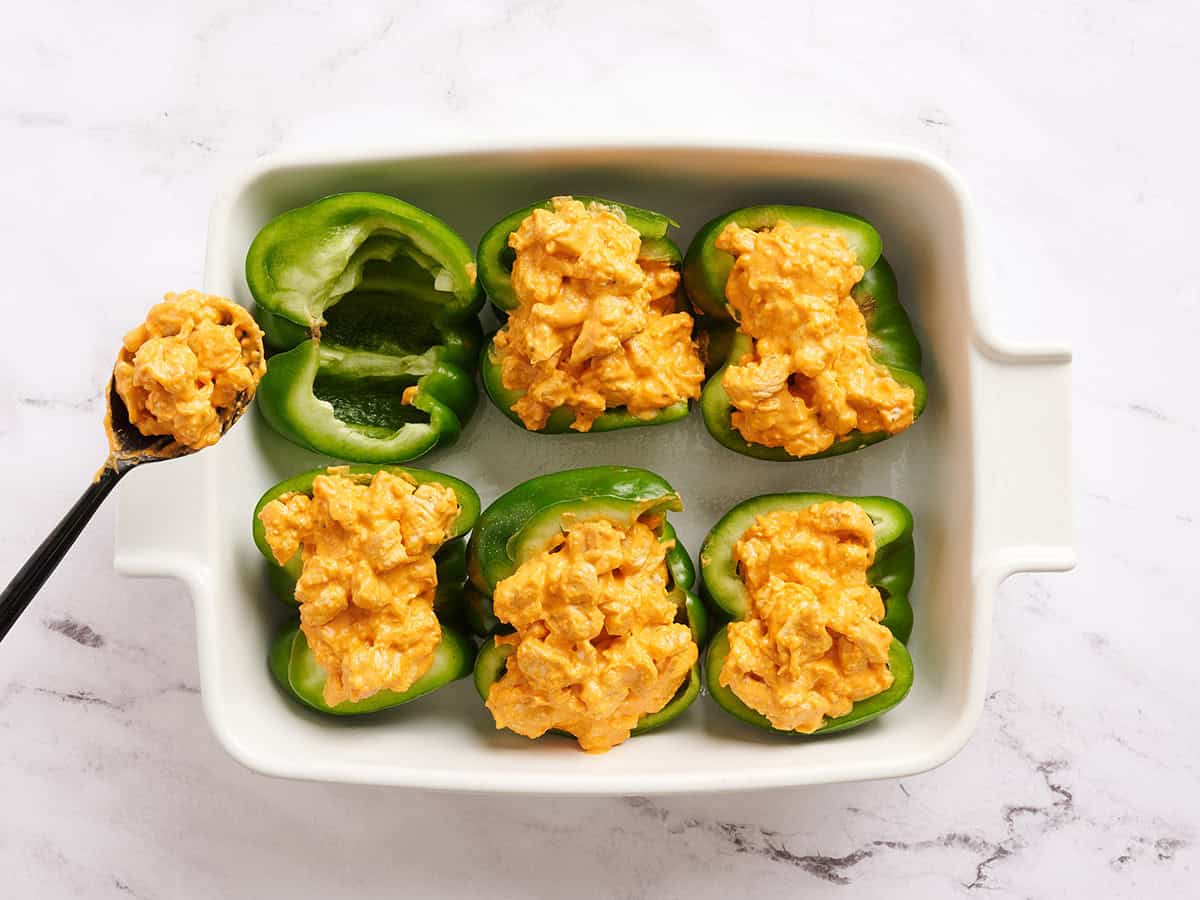 Moitiés de poivron vert dans un plat allant au four avec garniture au poulet Buffalo ajoutée.