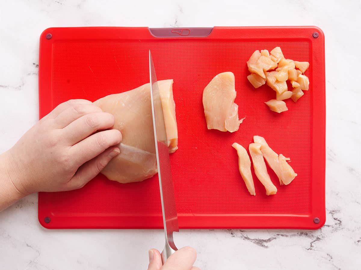 Une main utilisant un couteau pour couper la poitrine de poulet en morceaux.
